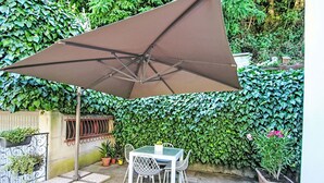 Une terrasse avec une table et des chaises, un grand parasol et un mur recouvert de verdure.