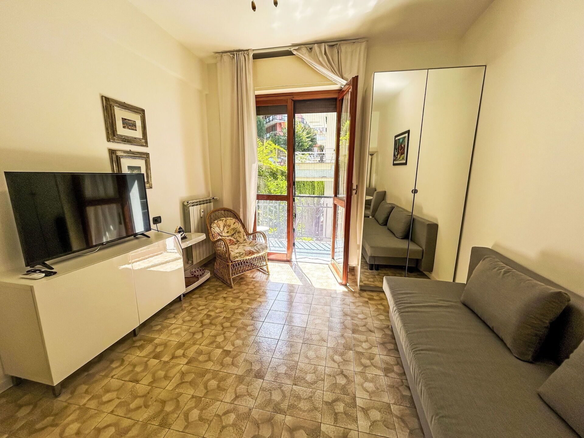 A living room with a flat-screen TV, a sofa, a chair, and a balcony with a view of the outside.