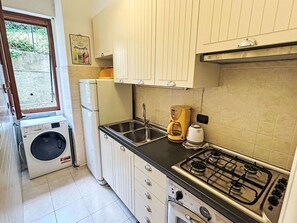 A compact kitchen with a washing machine, a sink, a stove, and cabinets. - Nice apartment for 4 guests with A/C, WIFI, TV and patio (Rapallo)