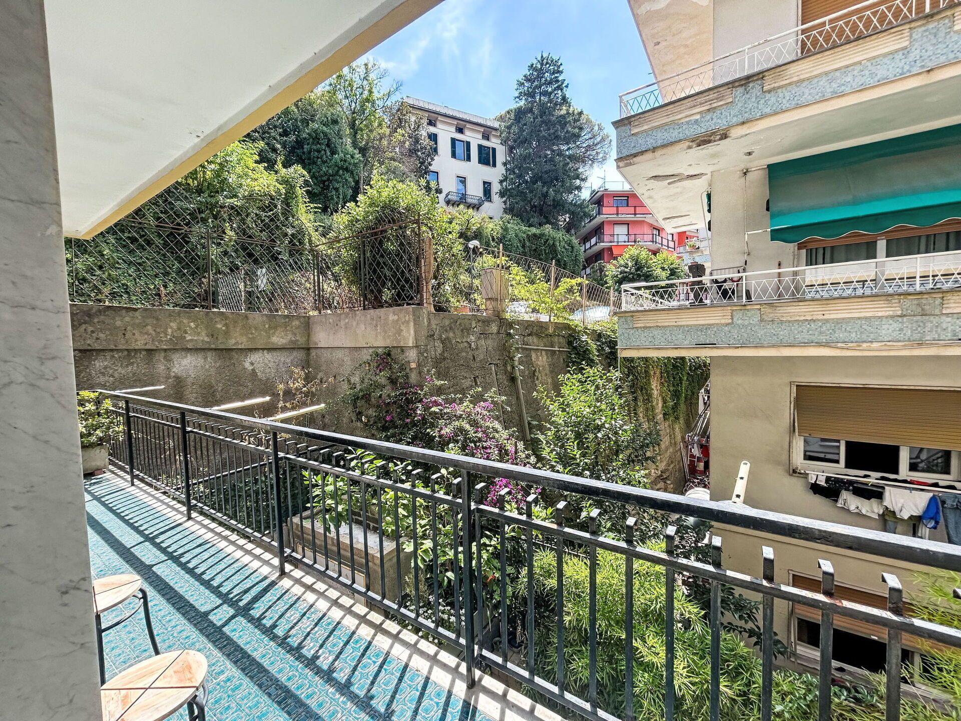 A balcony with a view of a courtyard, a pool, and buildings in the background.