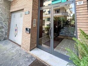 Ein Gebäudeeingang mit einer steinernen Fassade, einem Metallgitter und einer Glastür, die auf einen Balkon führt.