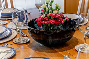 Ein Esstisch, gedeckt mit Tellern, Besteck und einer Blumenschale mit roten und weißen Blumen.