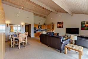 Ein geräumiges Wohnzimmer mit einer Couch, ein Essbereich mit Stühlen und einem Tisch, eine Küche mit Holzausstattung und ein Fernseher im Wohnbereich.