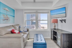 Ein Wohnzimmer mit einer Couch, einer Bank, einem Fernseher und einem Fenster mit Blick auf den Strand.