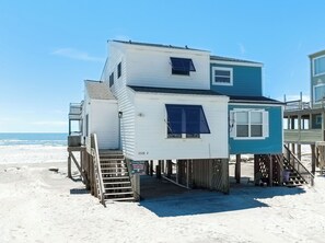 Ein mehrgeschossiges Strandhaus mit einer Treppe zum Haupteingang, einer kleinen Veranda und Blick auf den Ozean.
