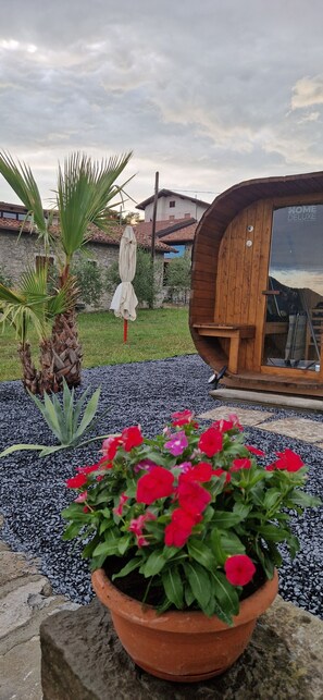 Ein Garten mit einer Palme, einem Topfpflanzen mit roten Blüten und einer Holzhütte mit einem Schild.