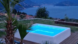 A rectangular swimming pool with a wooden deck in the foreground, surrounded by greenery and a view of a lake and mountains in the background. - Corte Furmignano 🏡 A farmhouse surrounded by greenery with a spectacular view of the lake (Esmate)