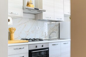 Eine moderne Küche mit weißen Schränken, einer Marmor-Spritzschutzleiste, einem Gasherd und einem eingebauten Backofen.