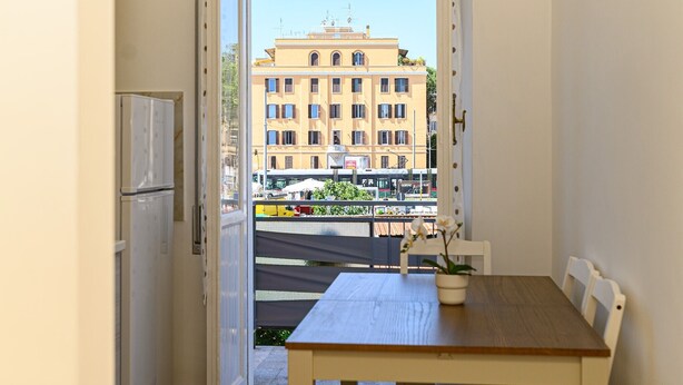 A balcony with a table and chairs, a potted plant, and a view of a building with multiple windows. - Monteverde Marí House Vacation Home with Wi-Fi (Rome)