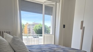 A bedroom with a bed, a bedside table with a lamp, a radiator, and a window with blinds. - Monteverde Marí House Vacation Home with Wi-Fi (Rome)