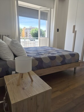 Ein Schlafzimmer mit einem Bett, einem Nachttisch mit Lampe, einem Heizkörper und einem Fenster mit Jalousien.