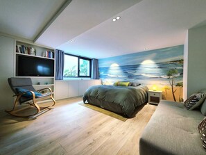 Ein Schlafzimmer mit einem Bett, einem Schaukelstuhl, einem Bücherregal, einem Fernseher und einem großen Fenster.