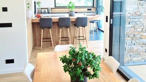 Un espace repas moderne avec une table en bois, quatre chaises, une plante en pot et un grand luminaire suspendu.