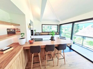 Eine moderne Küche mit einer Holztischinsel, Barhocker, einem großen Fenster und Blick ins Freie.