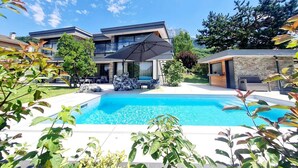 Une maison moderne à deux étages, dotée d’une piscine, d’un espace salon extérieur et offrant une vue sur les montagnes.