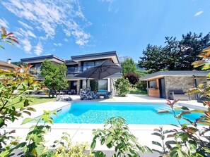 Ein modernes, zweistöckiges Haus mit Swimmingpool, Gartenmöbeln und Bergblick.