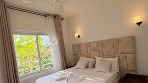 Un dormitorio con cama, ventilador de techo, ventana con cortinas y dos luces fijadas a la pared.