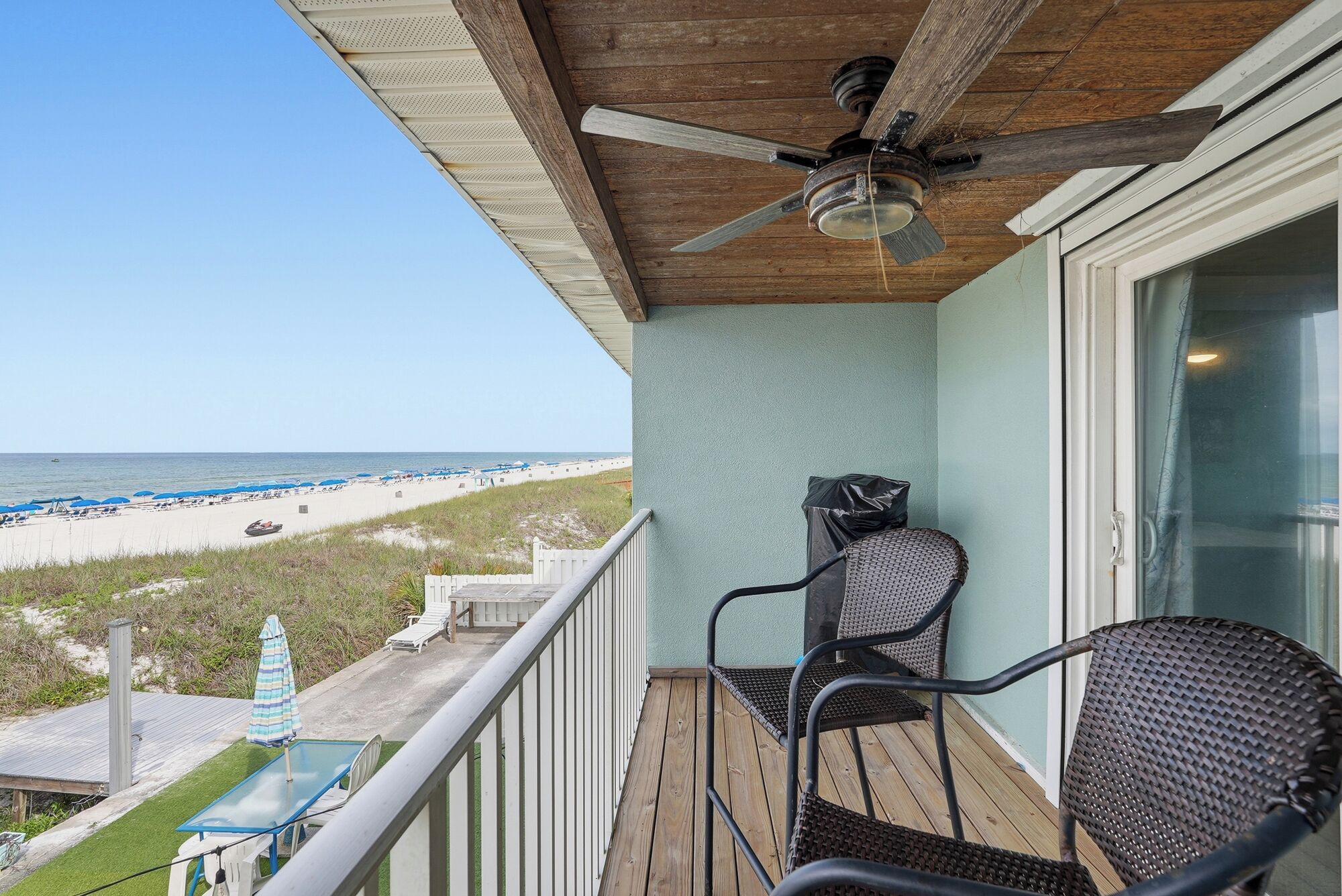 Un balcon avec vue sur la plage, un ventilateur de plafond et une chaise.