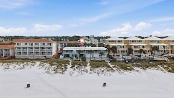 Un hotel frente a la playa con edificios de varios pisos, piscina y una playa de arena.