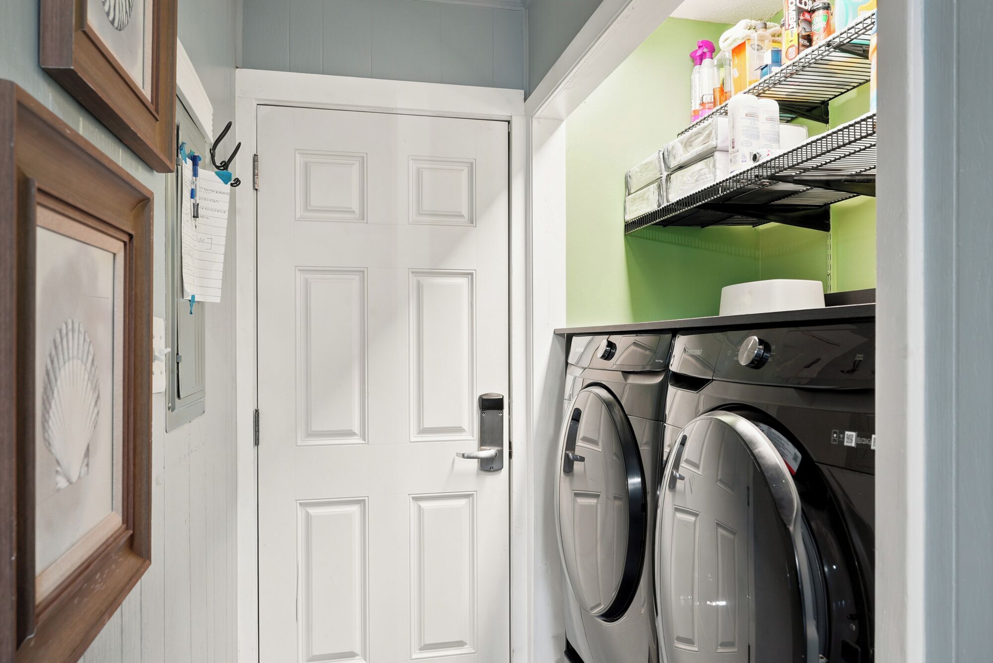 A laundry room with a white door, two front-loading washing machines, and shelves with various items.