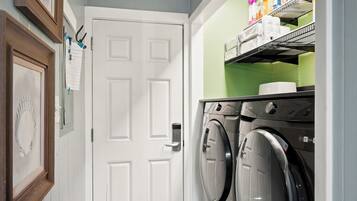 A laundry room with a white door, two front-loading washing machines, and shelves with various items.