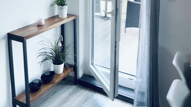 A room with a sliding glass door, a wooden console table with potted plants, and a view of the outside.