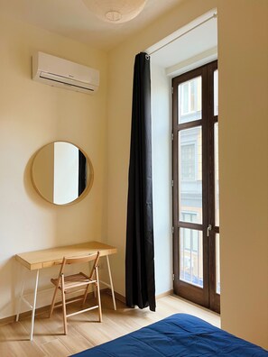 Ein Zimmer mit Schreibtisch, Stuhl, Spiegel, Klimaanlage, schwarzem Vorhang und einer Tür zu einem Außenbereich.