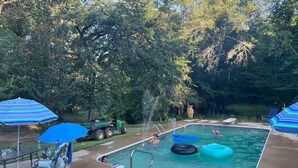 A swimming pool with inflatable rings, surrounded by trees and blue umbrellas. - River Retreat (Valliant)