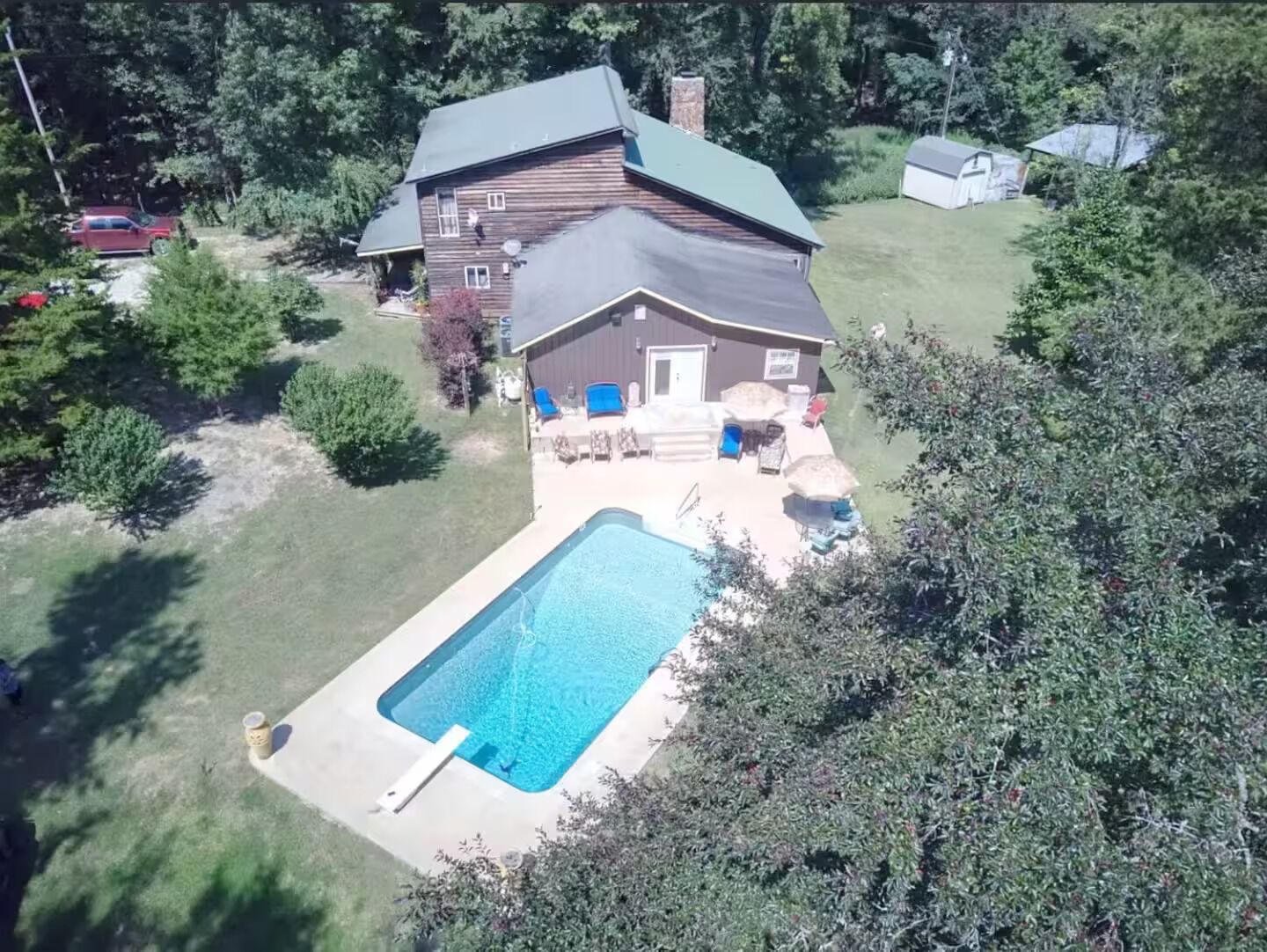 A two-story house with a swimming pool, surrounded by trees and a grassy yard.