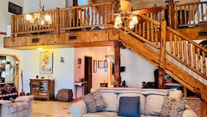 A spacious living area with a high ceiling, a wooden staircase, and a comfortable sofa. - River Retreat (Valliant)