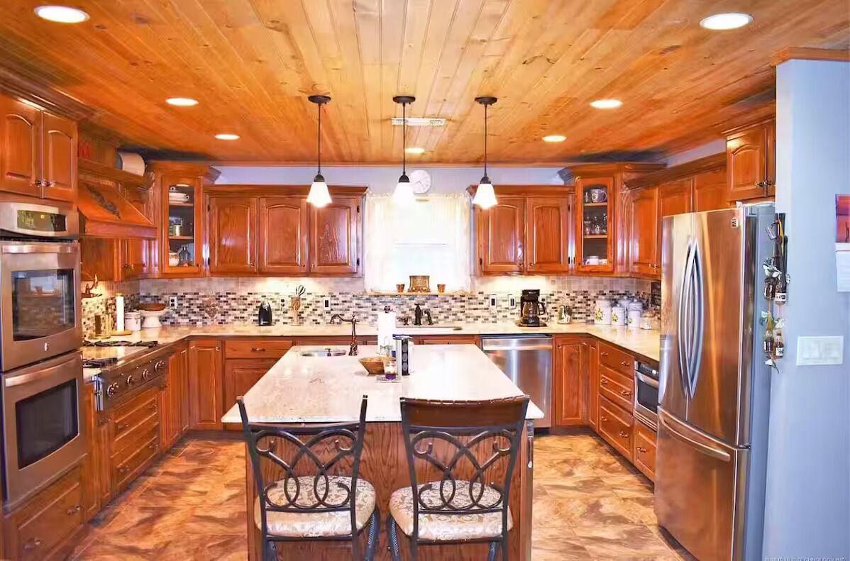 A kitchen with wooden cabinets, a central island, stainless steel appliances, and pendant lighting.
