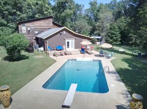 A rectangular swimming pool with a diving board, surrounded by a patio with outdoor furniture. - River Retreat (Valliant)