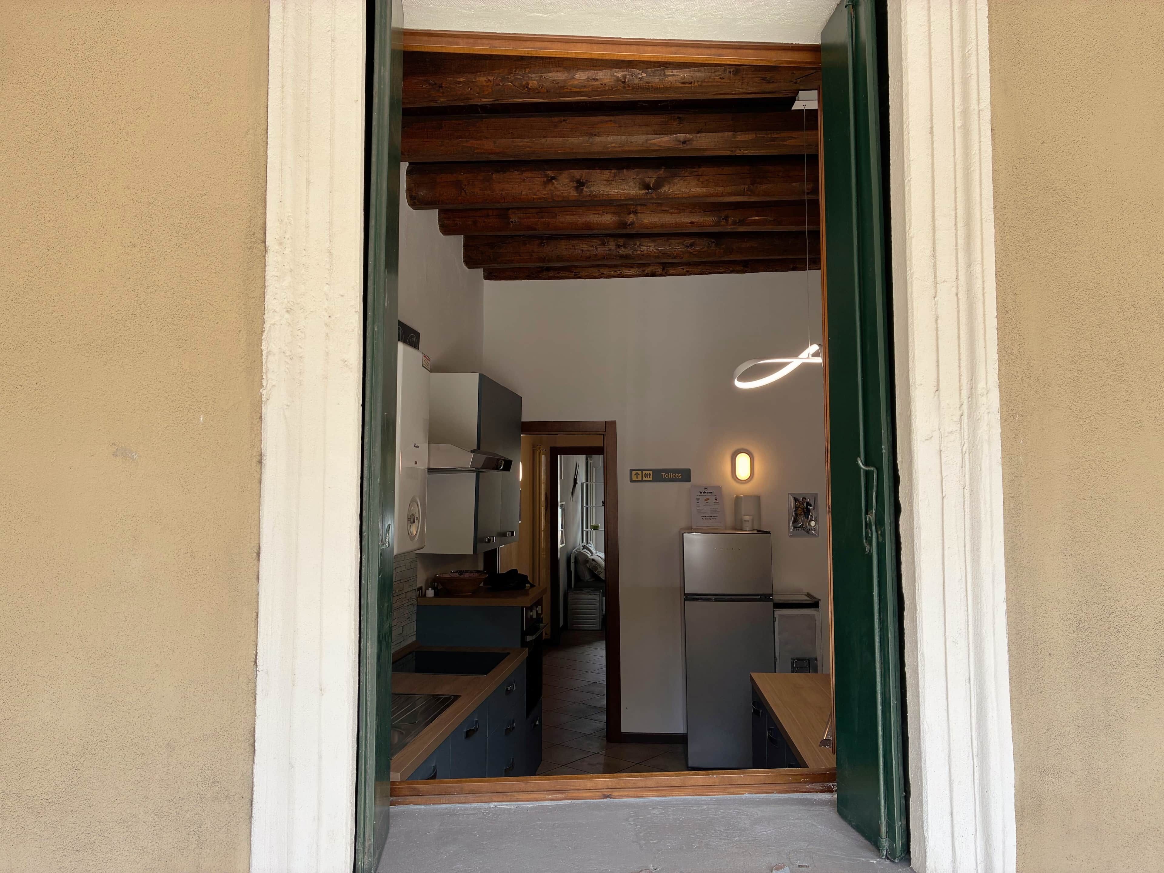 A narrow hallway leading to a kitchen with wooden beams, a refrigerator, and a sink.