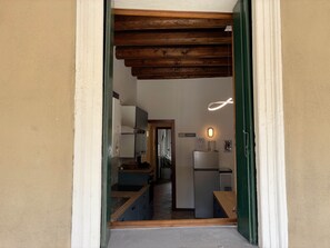 A narrow hallway leading to a kitchen with wooden beams, a refrigerator, and a sink.