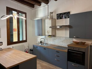 A modern kitchen with a built-in oven, a sink, and a window with wooden frames.