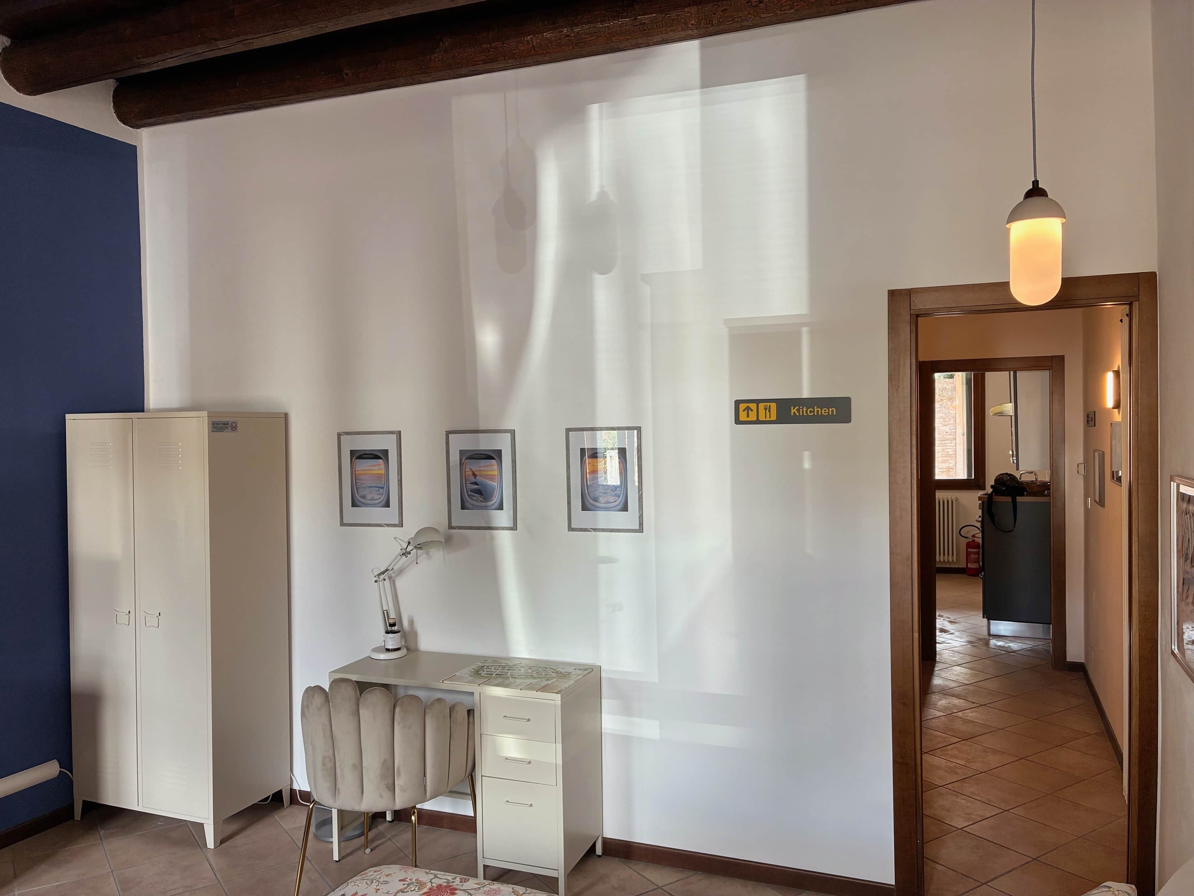 A room with a desk, chair, radiator, and a sign indicating the kitchen.