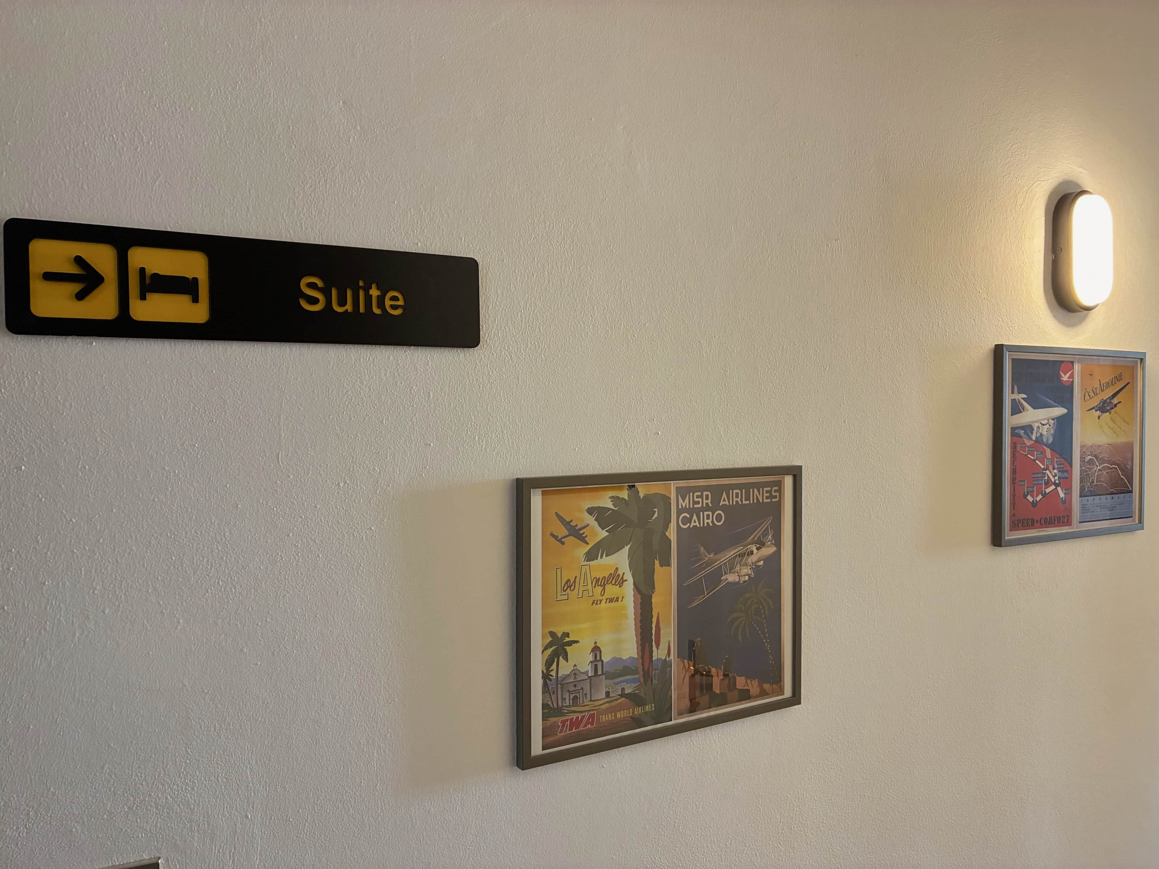 Señal que indica la dirección de una suite, un cartel antiguo de una aerolínea en marco y un aplique de pared.