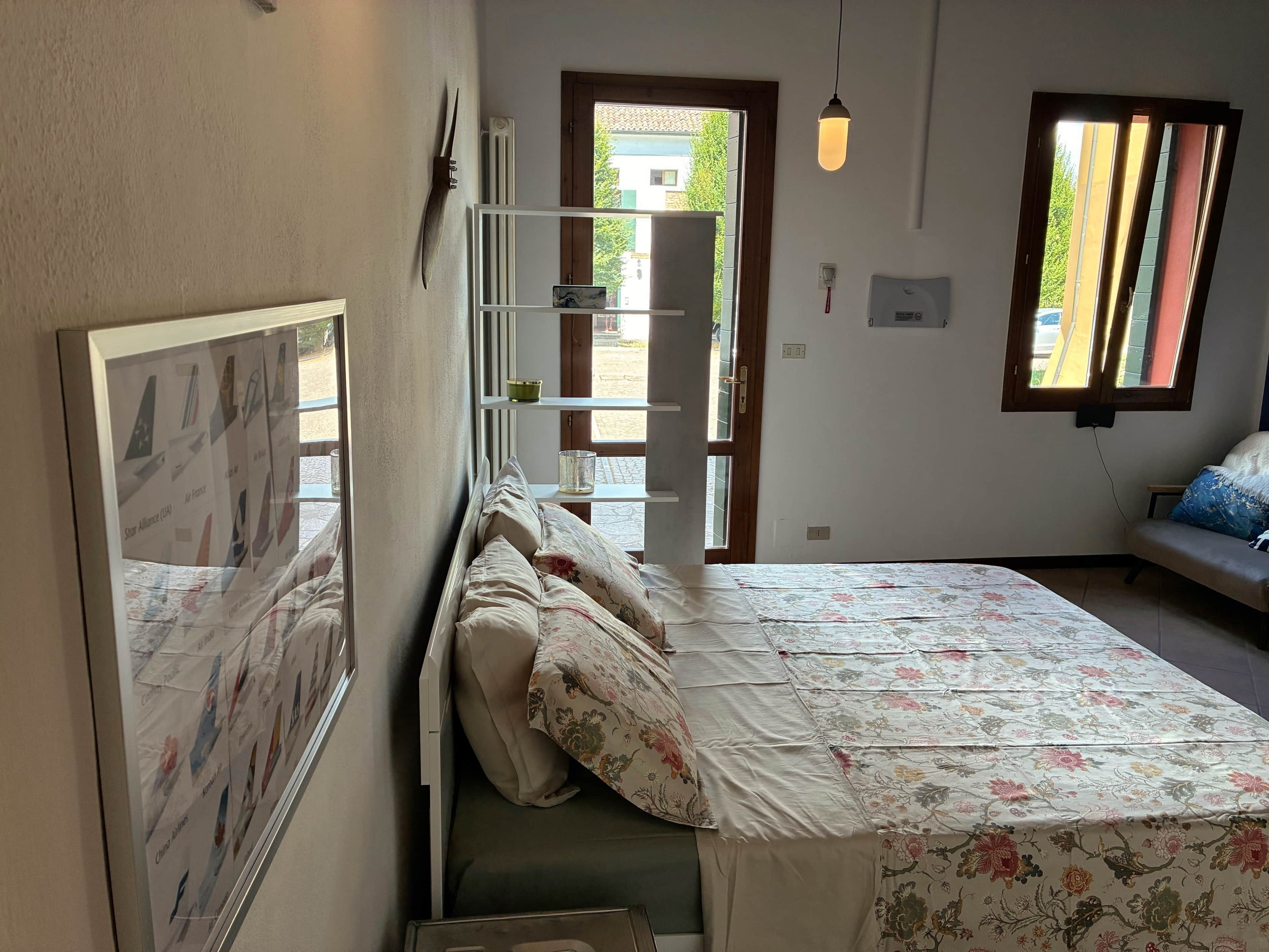 Une chambre à coucher comprenant un lit, une table de chevet, un miroir, une fenêtre avec des rideaux et une vue sur l’extérieur.