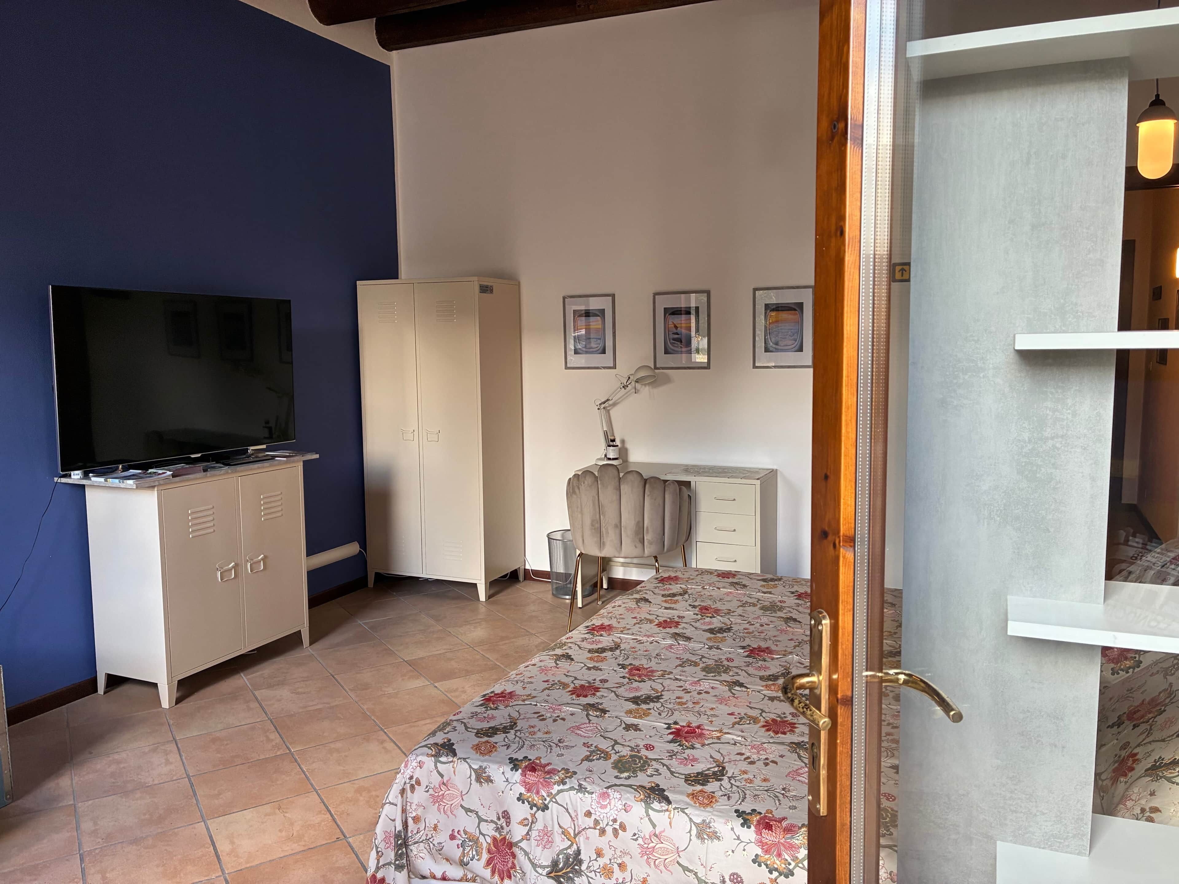 A bedroom with a bed, a TV, a wardrobe, a desk, and a lamp.
