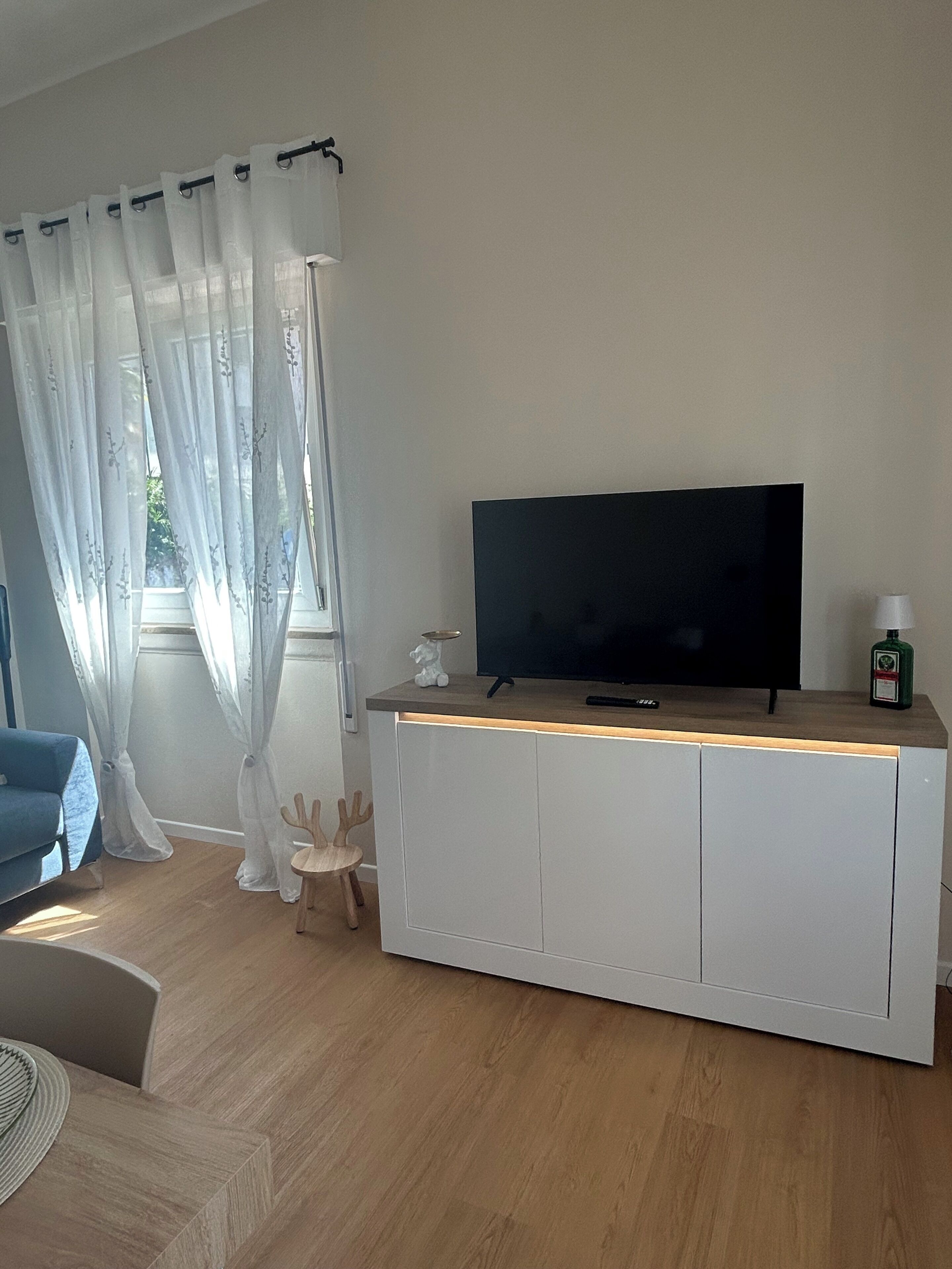 A modern living room with a flat-screen TV on a white cabinet, a blue sofa, and a wooden coffee table.