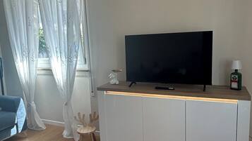 A modern living room with a flat-screen TV on a white cabinet, a blue sofa, and a wooden coffee table.