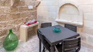 Un patio con una mesa y sillas, un muro de piedra, una planta verde y un letrero de bienvenida.