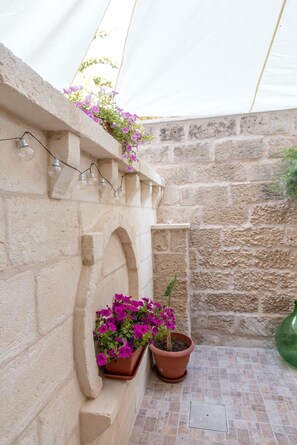 A stone wall with a built-in planter holding purple flowers, a potted plant, and a string of lights. - Apartment 'Rondinella By Palazzo Refolo' with Private Garden, Wi-Fi and Air Conditioning (Martano)
