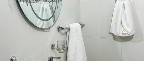 Une salle de bain avec un miroir rond, un lavabo blanc, un distributeur de savon en verre et un porte-serviettes avec deux serviettes.