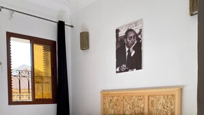 Huone, jossa on sänky, puinen pääty, yöpöytä, seinälle ripustettu taulu ja ikkuna, josta on näkymä.