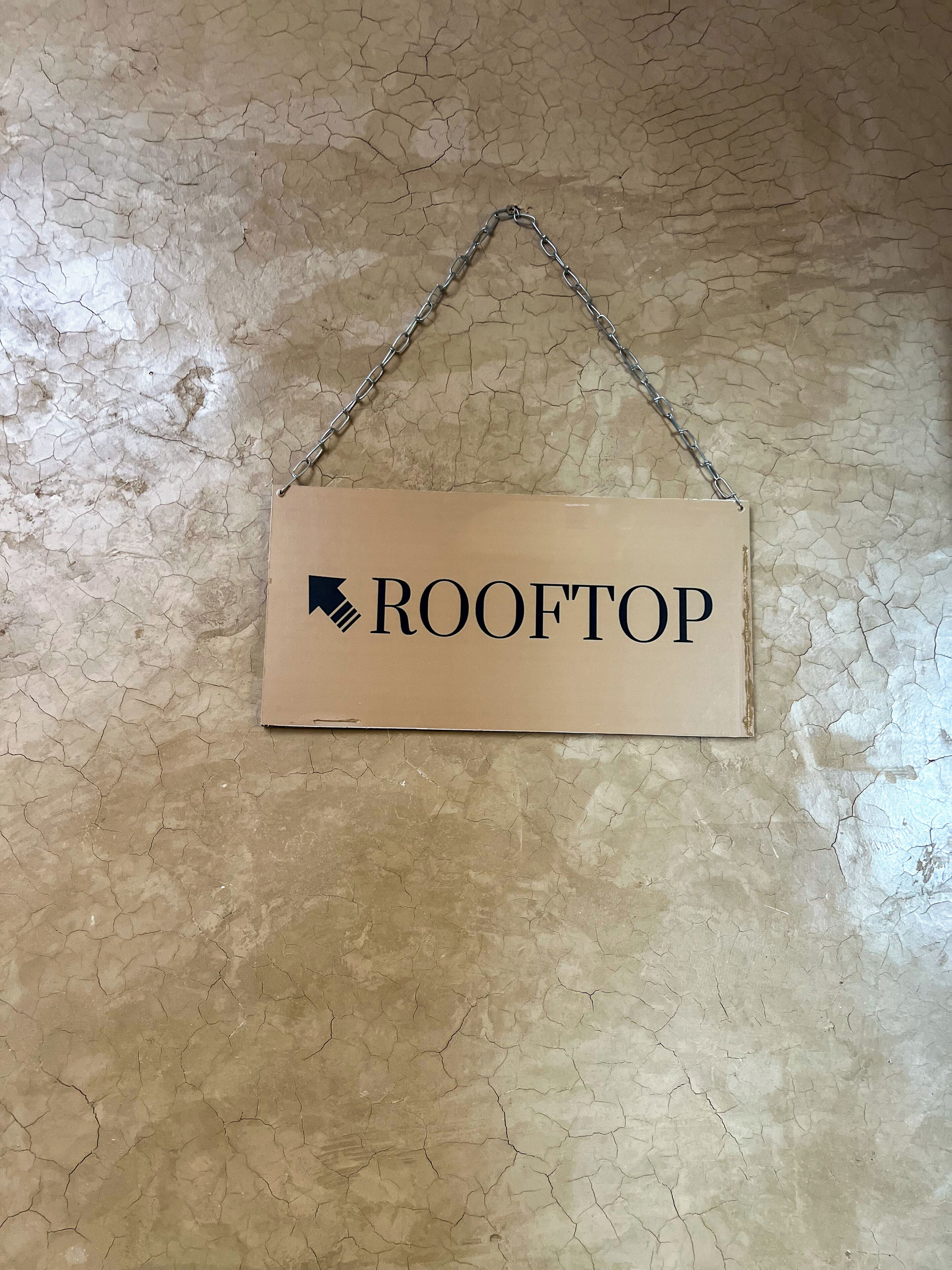 A sign with the word 'ROOFTOP' and a downward arrow, hanging on a textured wall.