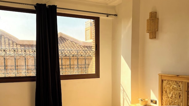 Un dormitorio con una cama grande, una ventana con cortinas, vista a un edificio y una mesita con una cesta.