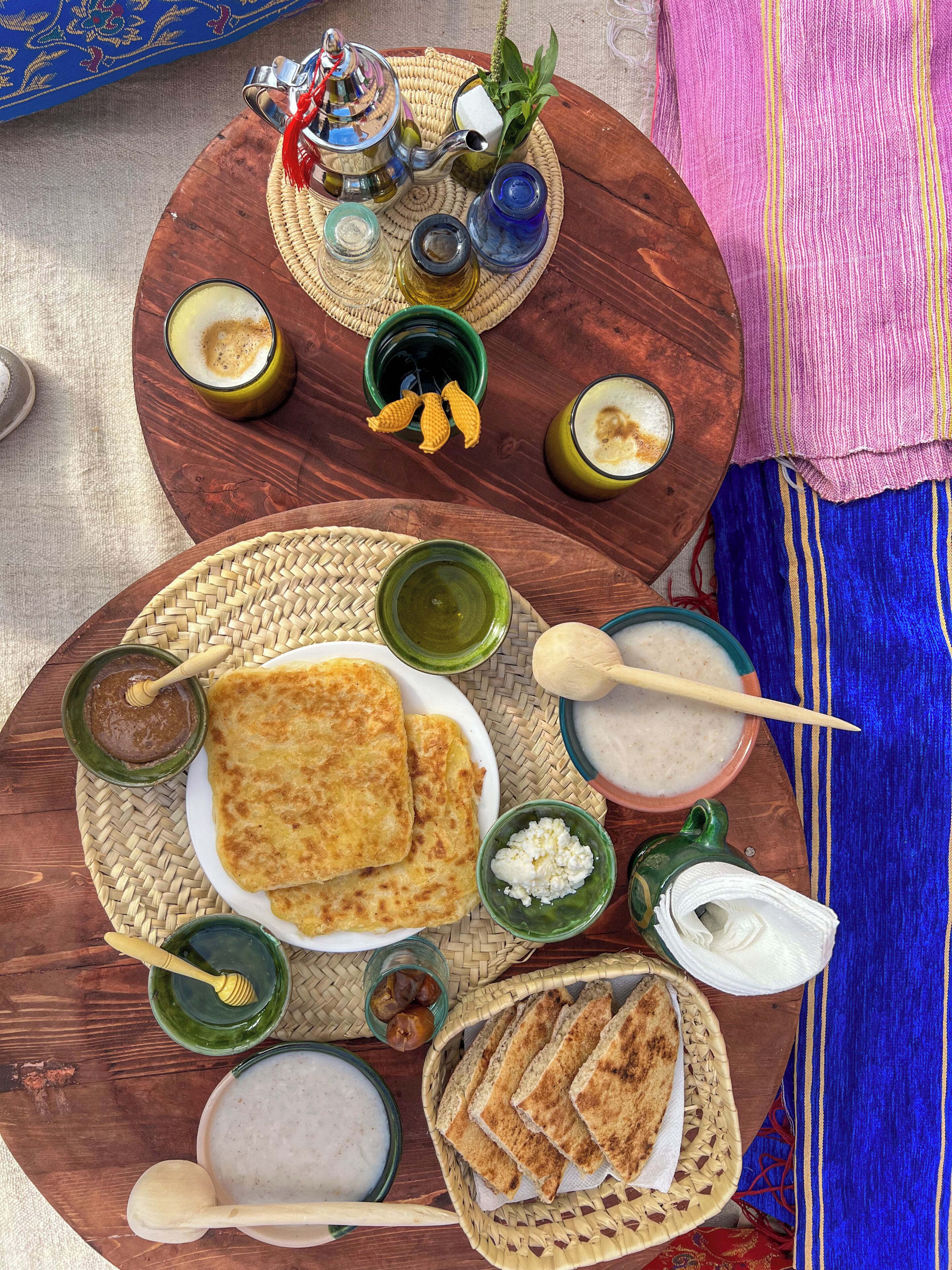 A wooden table with various food items and utensils, including flatbreads, dips, and a teapot.