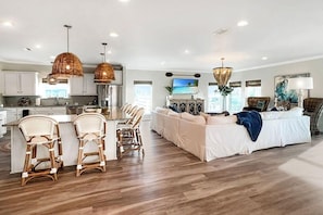 A spacious living area with a large sofa, a dining area with wicker chairs, and a kitchen with white cabinets. - Front and Sea (Port St. Joe)