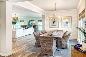 A dining area with a wooden table and wicker chairs, a chandelier, and framed artwork on the wall. - Front and Sea (Port St. Joe)